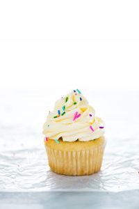 Gluten Free Vanilla Cupcakes with a single cupcake with vanilla frosting and sprinkles