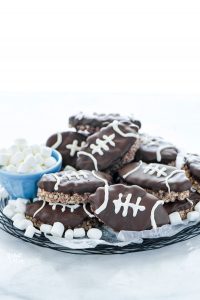 Football Rice Krispie Treats on a wax paper lined wire plate garnished with mini marshmallows