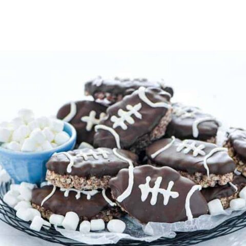 Football Rice Krispie Treats on a wax paper lined wire plate garnished with mini marshmallows