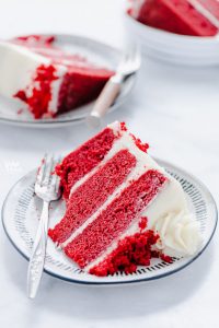 A slice of Gluten Free Red Velvet Cake on a small white plate with a bite taken out