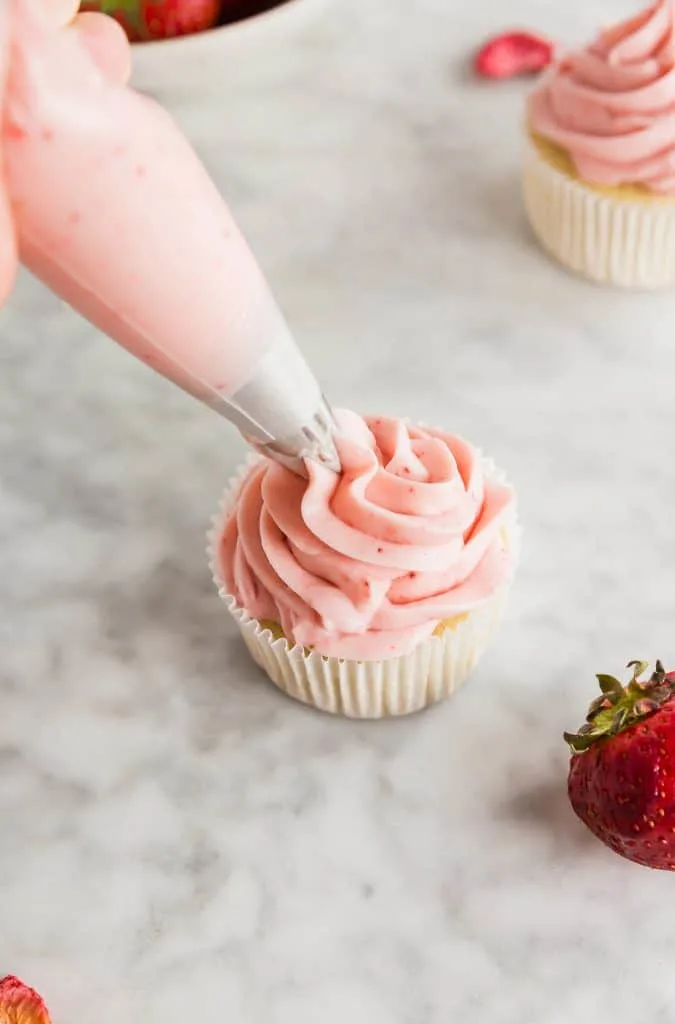 Strawberry Cream Cheese Frosting being piped onto a vanilla cupcakes