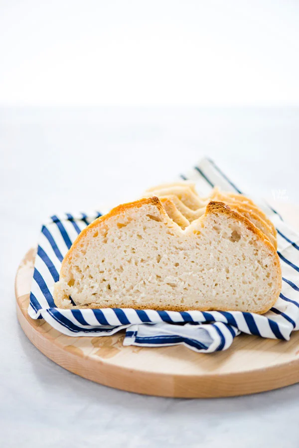 sliced gluten free sourdough bread on top of a white and blue striped napkin on a round wood cutting board