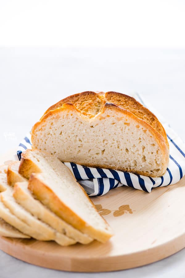 Half sliced Gluten Free Sourdough Bread on a white and blue striped napkin on a round wood cutting board