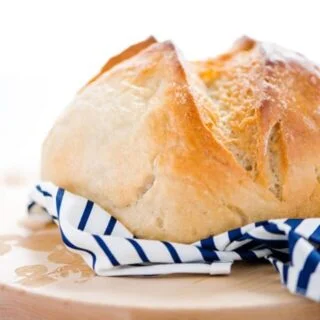 Gluten Free Sourdough Bread on a round wood cutting board with a blue and white striped napkin