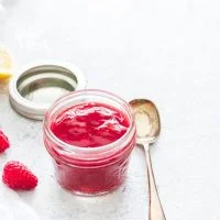 Homemade raspberry sauce in a small glass jar with a serving spoon nearby
