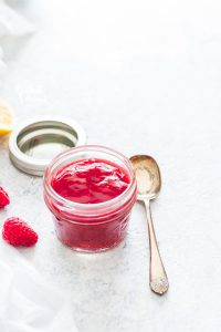 Homemade raspberry sauce in a small glass jar with a serving spoon nearby