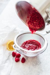 Freshly made raspberry sauce being poured into a mesh strainer to strain