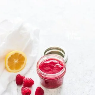 Raspberry Sauce in a small glass jar with fresh raspberries and half a lemon nearby