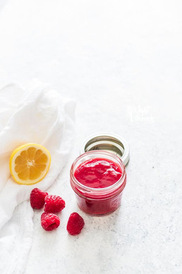 Raspberry Sauce in a small glass jar with fresh raspberries and half a lemon nearby