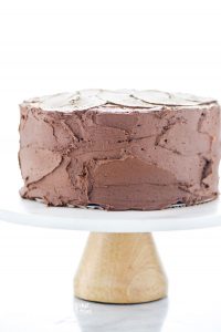 a baked and frosted gluten free sourdough chocolate cake recipe on top of a white cake stand with a light colored wood base