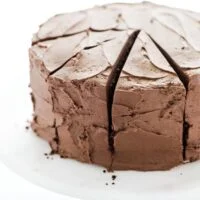 A frosted gluten free sourdough chocolate cake recipe on top of a white cake stand with a wood base.