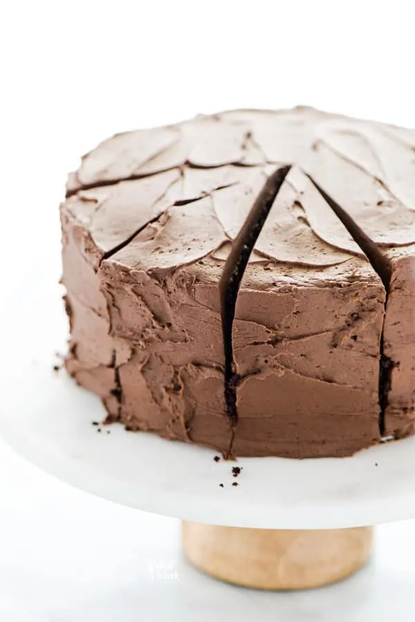 A frosted gluten free sourdough chocolate cake recipe on top of a white cake stand with a wood base. 