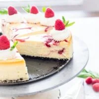 White Chocolate Raspberry Cheesecake on a cake stand with one slice missing, ready to be served