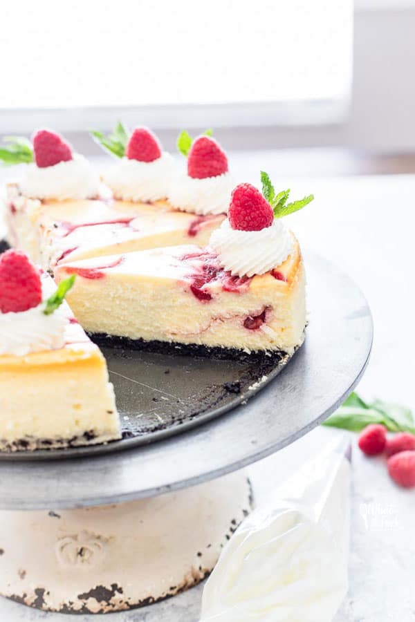 White Chocolate Raspberry Cheesecake on a cake stand with one slice missing, ready to be served