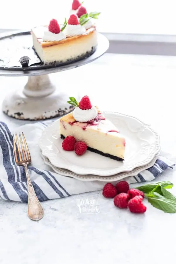 a slice of white chocolate raspberry cheesecake on a white plate on top of a white and blue striped towel