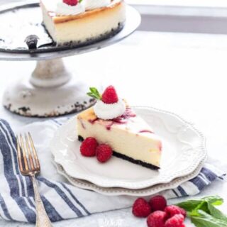 a slice of white chocolate raspberry cheesecake on a white plate on top of a white and blue striped towel
