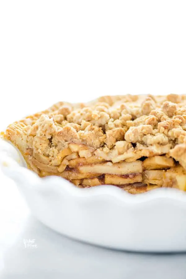 straight on shot of a gluten free apple crisp pie in a white pie dish, that's been cut into and served