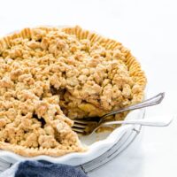 Apple crisp pie in a white pie dish with a piece removed and two forks in the spot of the missing slice of pie