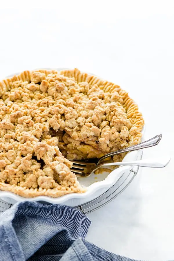Apple crisp pie in a white pie dish with a piece removed and two forks in the spot of the missing slice of pie