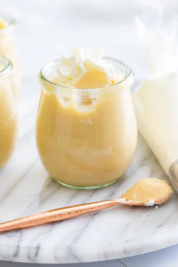 homemade maple pudding in a small glass jar topped with whipped cream with a bite removed