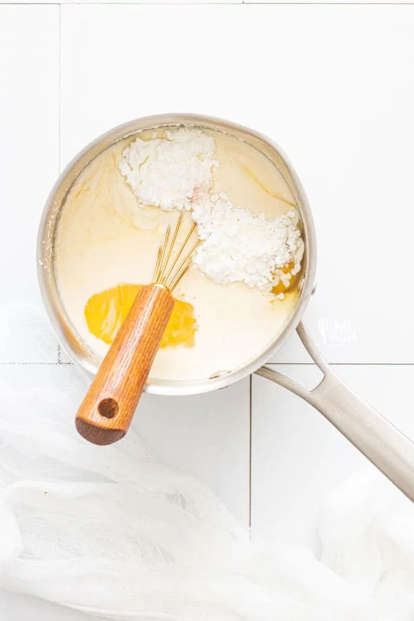 homemade maple pudding ingredients in a silver sauce pan with a wood handled whisk