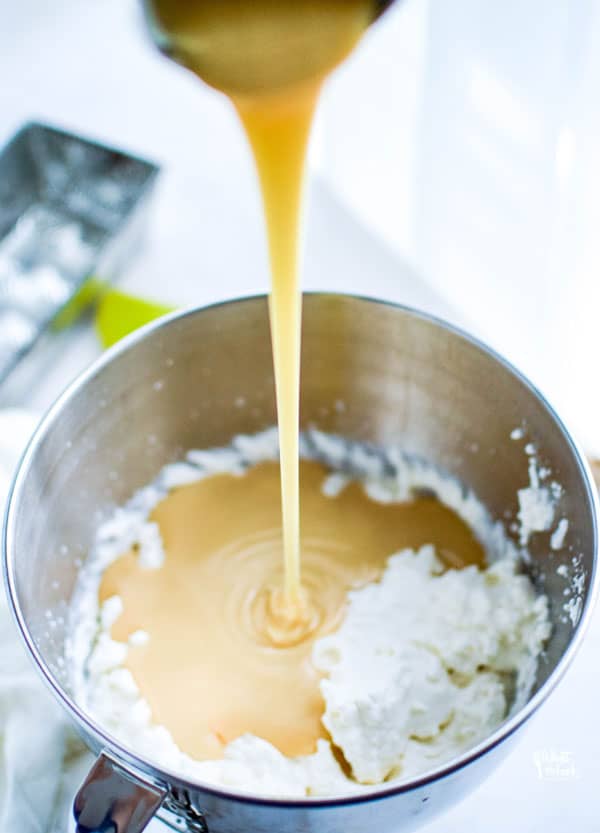 sweetened condensed milk being poured into a bowl of whipped cream to make no churn homemade vanilla ice cream
