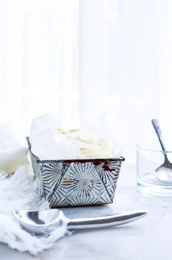 Homemade Vanilla Ice Cream in a silver loaf pan lined with parchment paper ready to be served