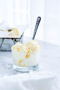 2 scoops of homemade vanilla ice cream in a glass bowl with a spoon sticking out
