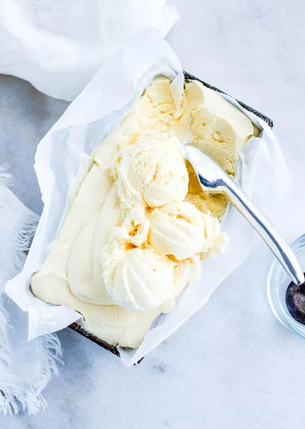 overhead shot of homemade vanilla ice cream in a silver loaf pan lined with white parchment paper that has started to be scooped