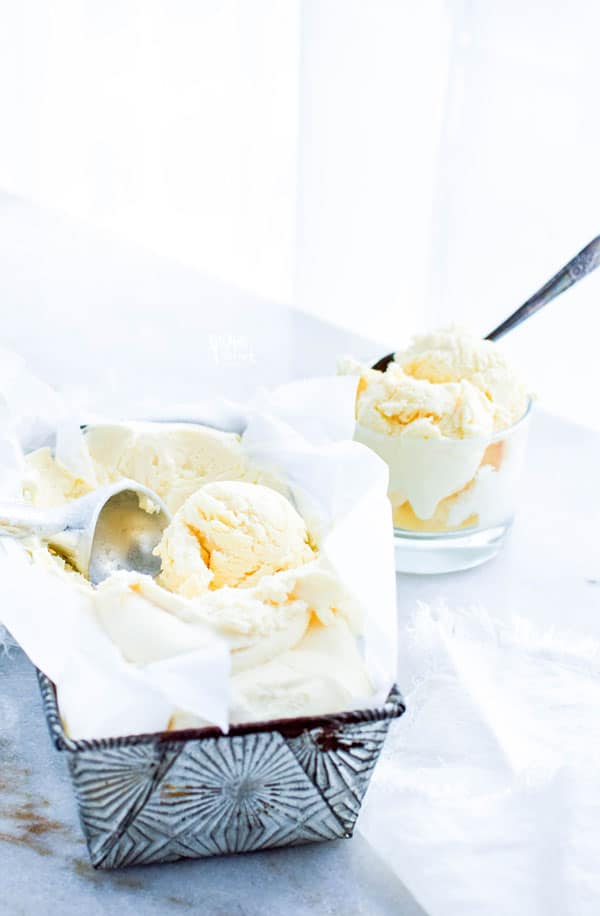 homemade vanilla ice cream being scooped from a silver pan with a bowl of ice cream already scooped in the background