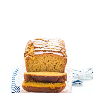 Sliced gluten free pumpkin spice bread on a small wood rectangular cutting board on top of a blue and white striped napkin