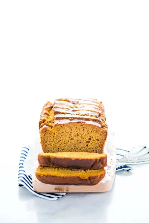 Sliced gluten free pumpkin spice bread on a small wood rectangular cutting board on top of a blue and white striped napkin