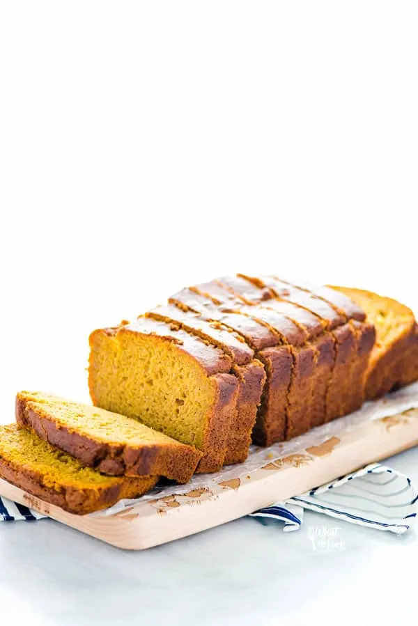 Sliced gluten free pumpkin spice bread on top of a light wood cutting board on top of a blue and white striped towel