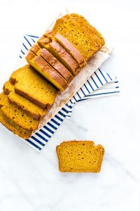 gluten free pumpkin spice bread sliced on a rectangular cutting board with one slice flat on a marble surface