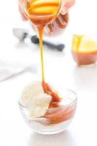 homemade salted caramel sauce being poured over a bowl of vanilla ice cream