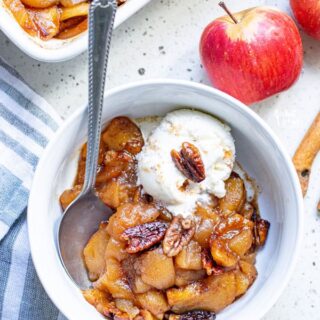cinnamon baked apple slices being served in a white bowl topped with a scoop of vanilla ice cream