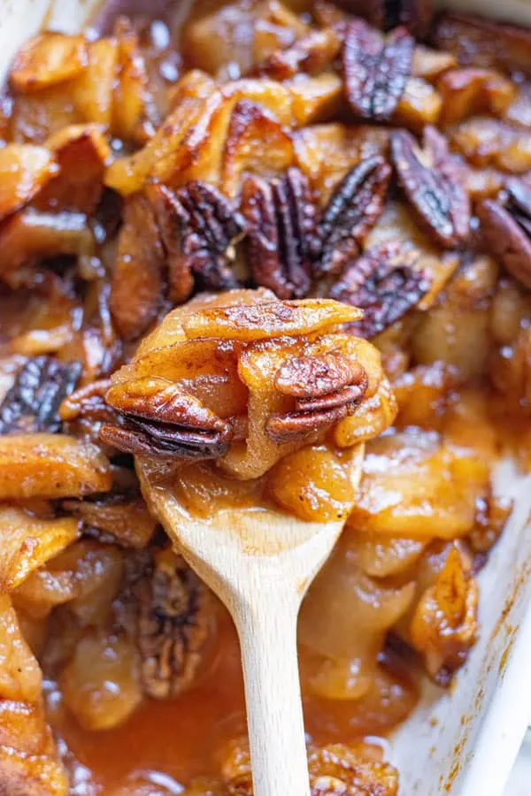 cinnamon baked apple slices being dished out of a white casserole dish with a wooden spoon