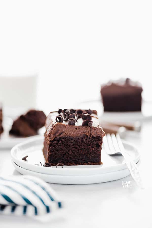 a slice of gluten free chocolate pumpkin cake on a stack of round white plates with a glass of milk and more slices of cake in the background