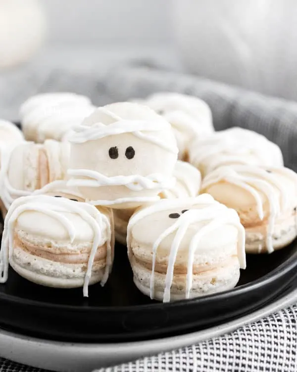 Mummy Macarons with Maple Cinnamon Filling on a black plate on top of a black and white cloth napkin