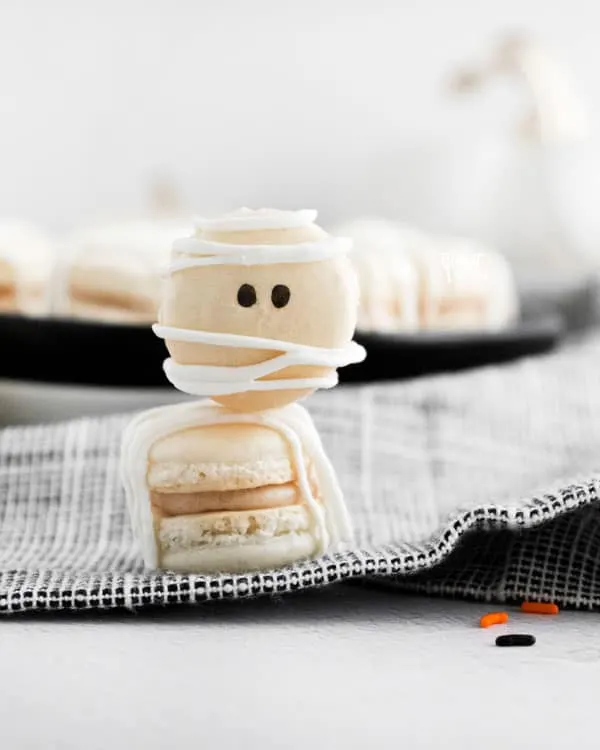 2 Mummy Macarons with Maple Cinnamon Filling stacked on top of each other on a black and white cloth napkin