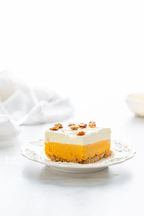 a slice of gluten free pumpkin lush cake on a white plate with a white linen crumpled in the background