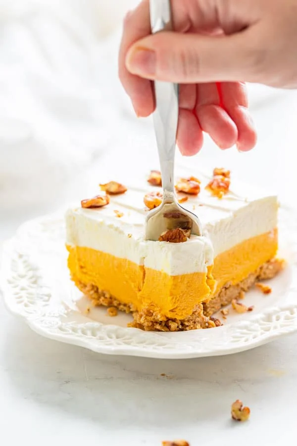 a slice of gluten free pumpkin lush cake on a white plate with a hand using a fork to remove a bite