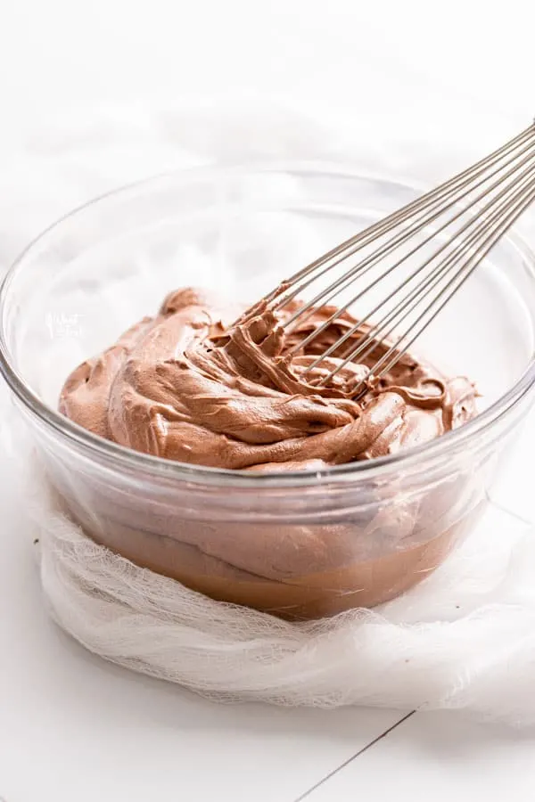 Chocolate Cream Cheese Frosting in a clear glass bowl being whisked