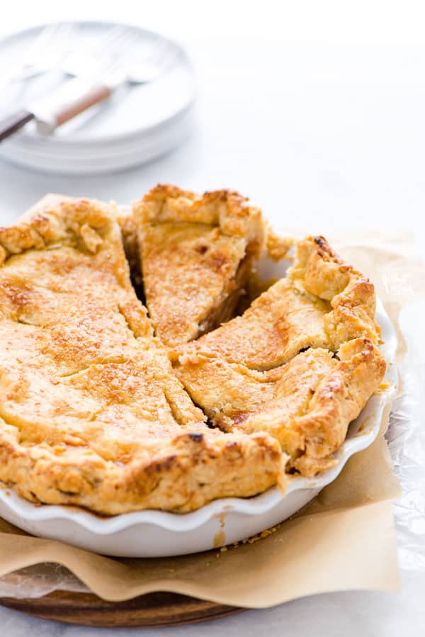 sliced GF apple pie in a white pie dish on top of brown parchment paper on a round wood pie board