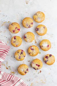 one dozen gluten free white chocolate cranberry muffins on a white board dusted with powdered sugar