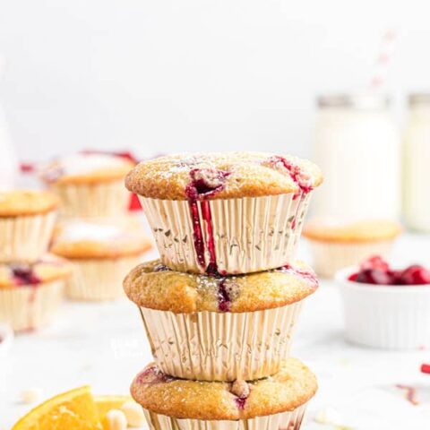 3 gluten free white chocolate cranberry muffins with silver liners stacked on top of each other