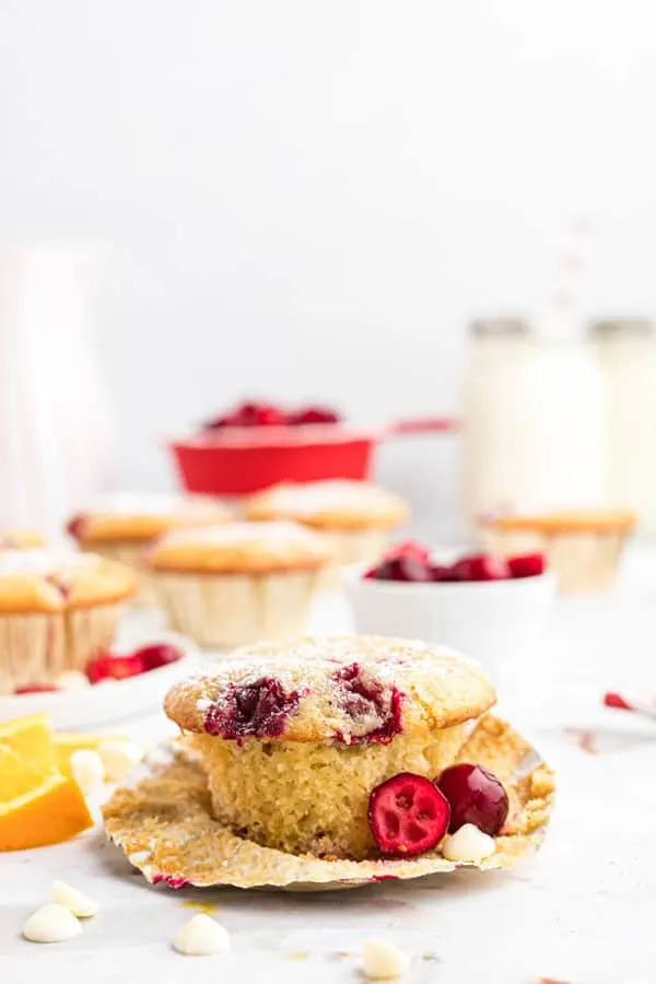 a gluten free white chocolate cranberry muffin in a paper liner that's starting to be unwrapped garnished with fresh cranberries