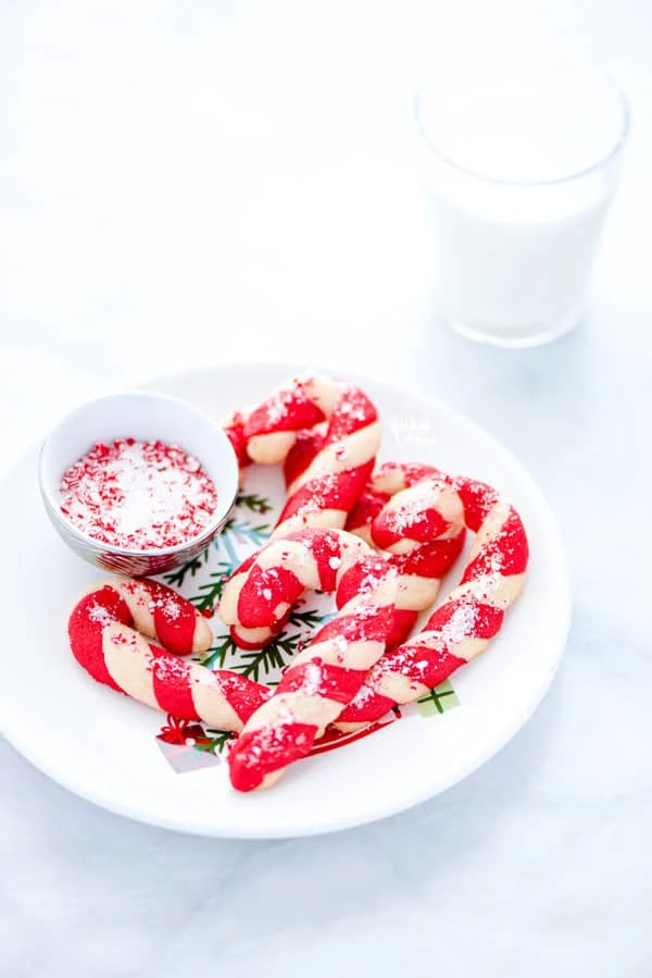 Gluten Free Candy Cane Cookies on a Christmas plate with a bowl of crushed candy canes and a glass of milk