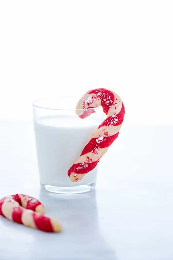 a gluten free candy cane cookie hanging on the side of a glass of milk