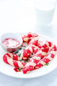 gluten free candy cane cookies on a white Christmas plate with a bowl of candy cane bits and a glass of milk in the background